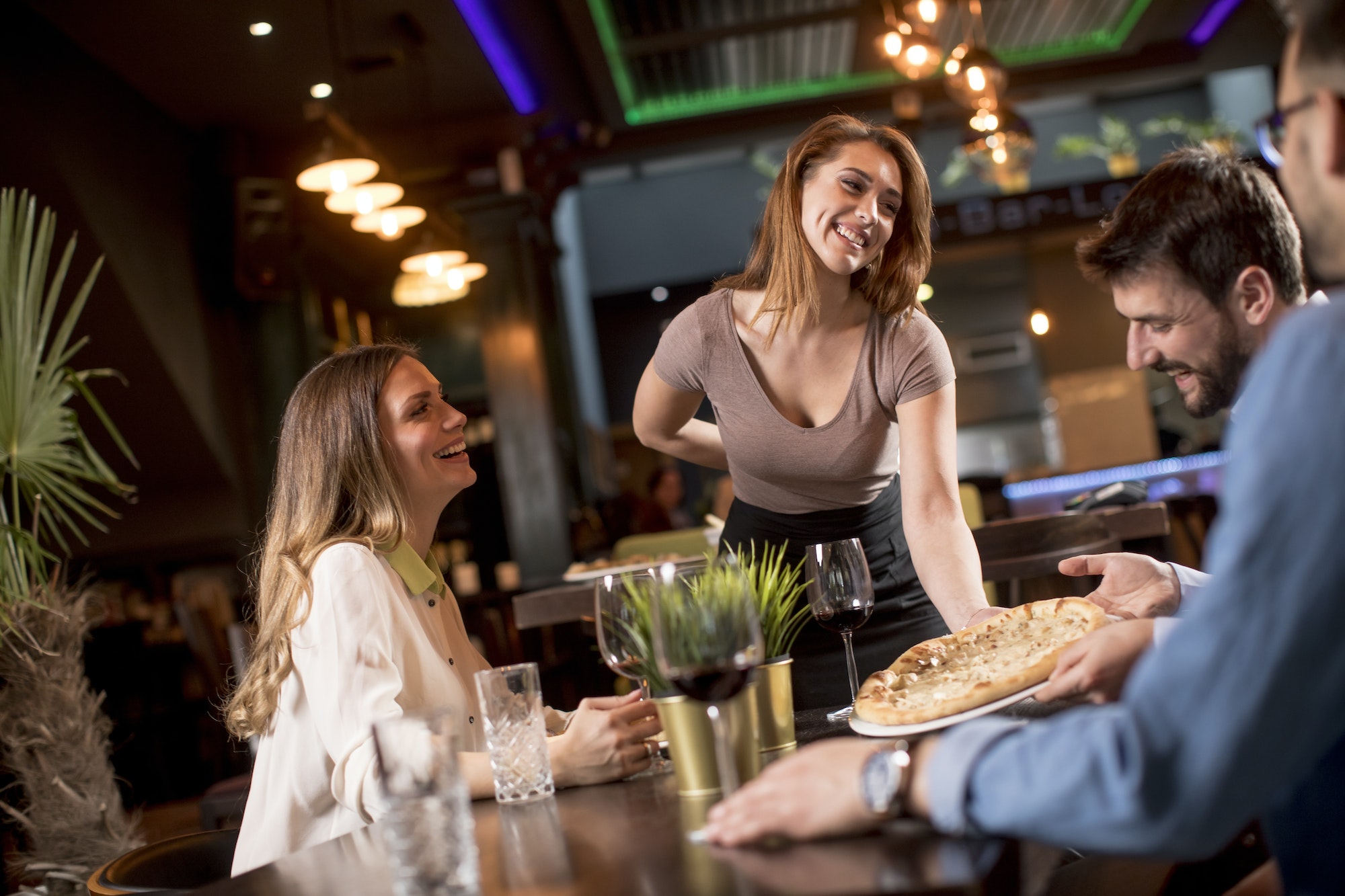 Waiter woman serving group of friends with food in the restaurant